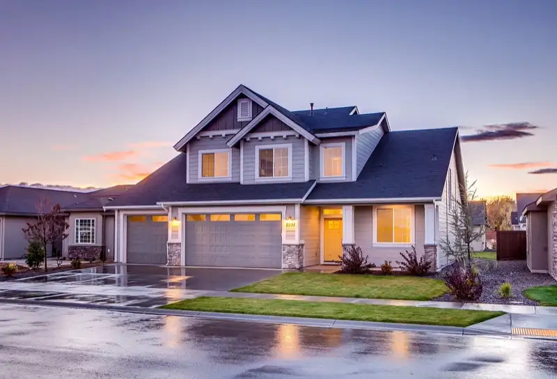 Two-story home photographed at twilight with warm interior lights and a reflective wet driveway